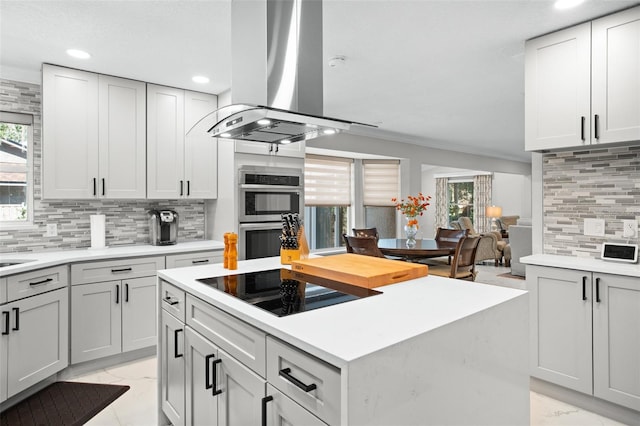 kitchen featuring gray cabinetry, backsplash, island exhaust hood, double oven, and black electric stovetop