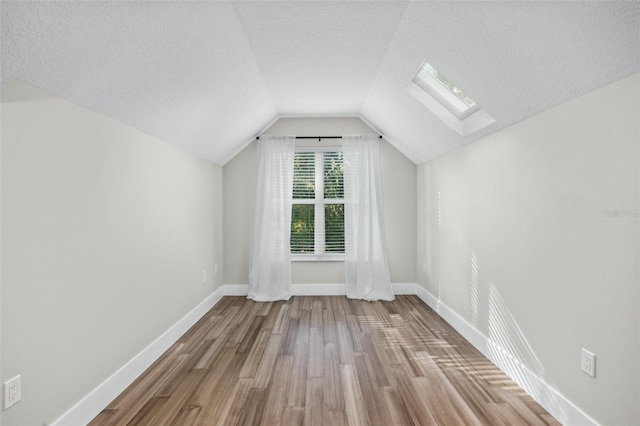 additional living space with vaulted ceiling with skylight, wood-type flooring, and a textured ceiling