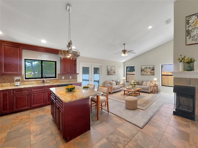 kitchen with pendant lighting, sink, vaulted ceiling, light stone countertops, and a kitchen island