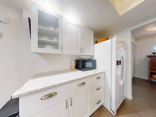 kitchen featuring light stone countertops, white cabinetry, and white refrigerator with ice dispenser