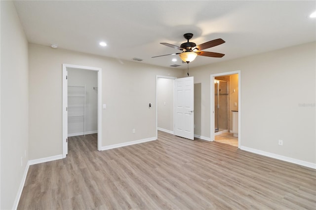 unfurnished bedroom with connected bathroom, a spacious closet, ceiling fan, a closet, and light wood-type flooring