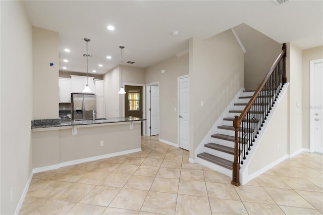 kitchen with kitchen peninsula, stainless steel fridge, decorative light fixtures, dark stone countertops, and white cabinets