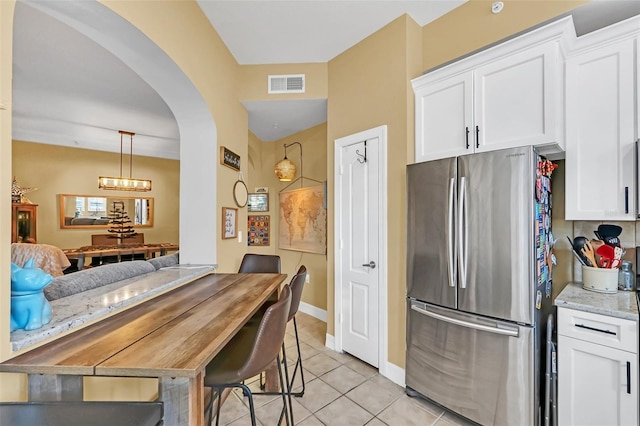 kitchen with white cabinets, stainless steel fridge, light stone counters, and light tile patterned floors