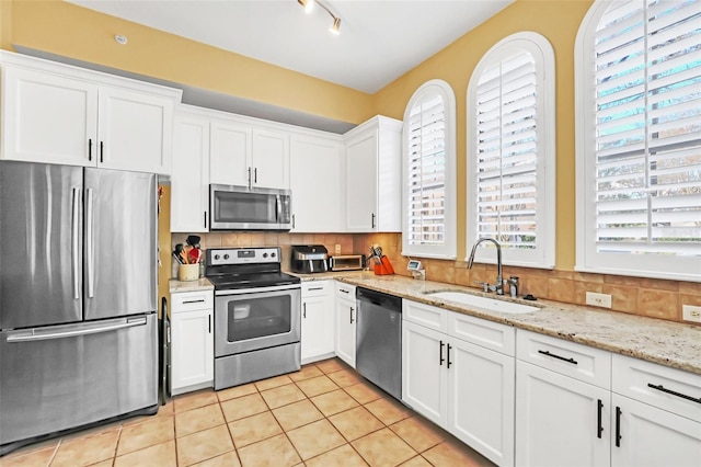 kitchen with tasteful backsplash, stainless steel appliances, sink, light tile patterned floors, and white cabinetry