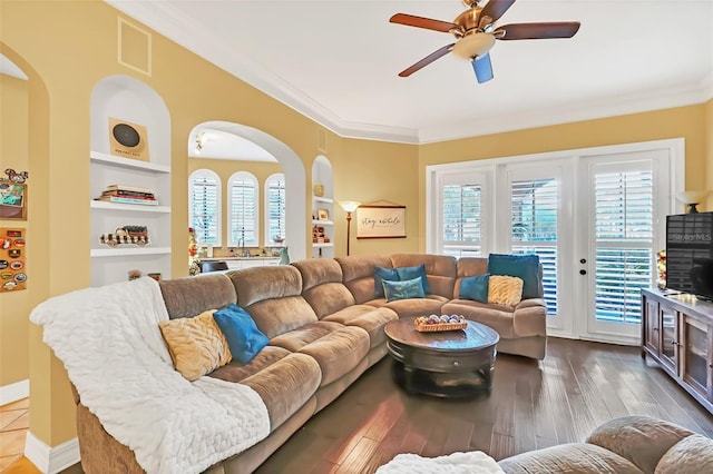 living room featuring built in shelves, dark hardwood / wood-style flooring, ceiling fan, and ornamental molding