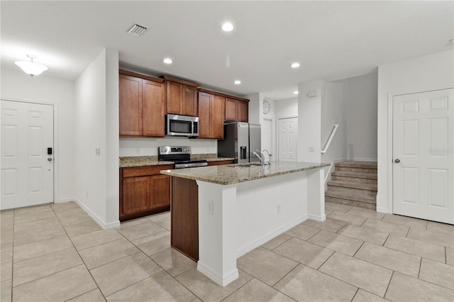 kitchen featuring light stone counters, an island with sink, light tile patterned floors, and appliances with stainless steel finishes