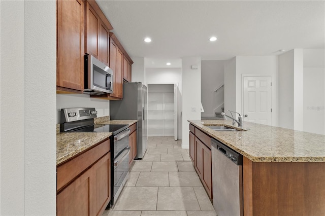 kitchen featuring light stone countertops, appliances with stainless steel finishes, sink, light tile patterned floors, and a center island with sink