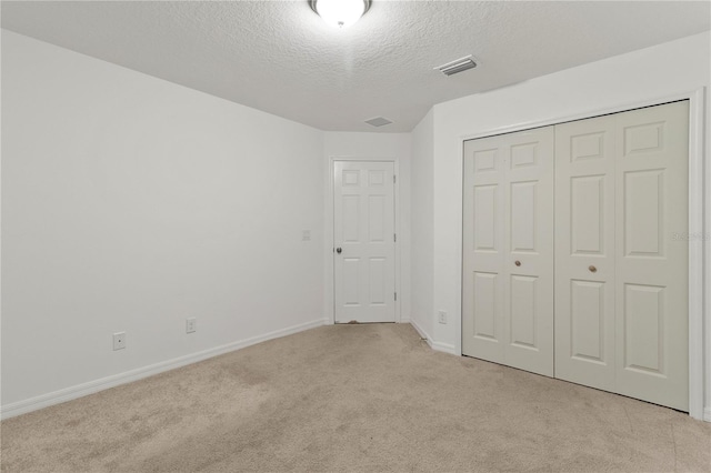 unfurnished bedroom featuring light carpet, a textured ceiling, and a closet