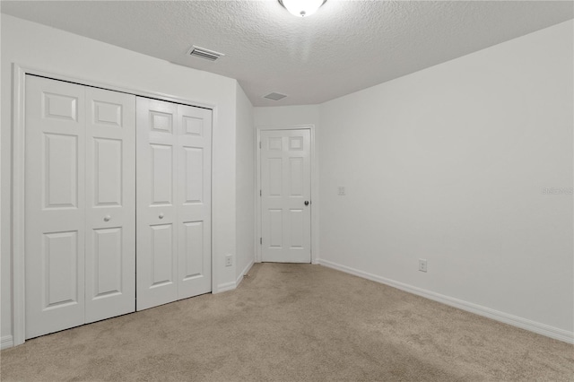 unfurnished bedroom featuring light colored carpet, a textured ceiling, and a closet