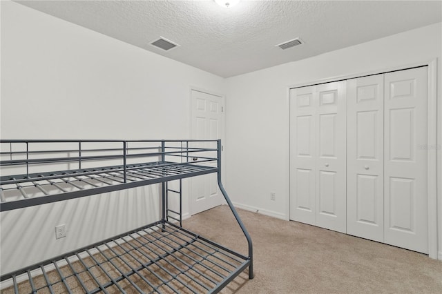 bedroom featuring light carpet, a textured ceiling, and a closet