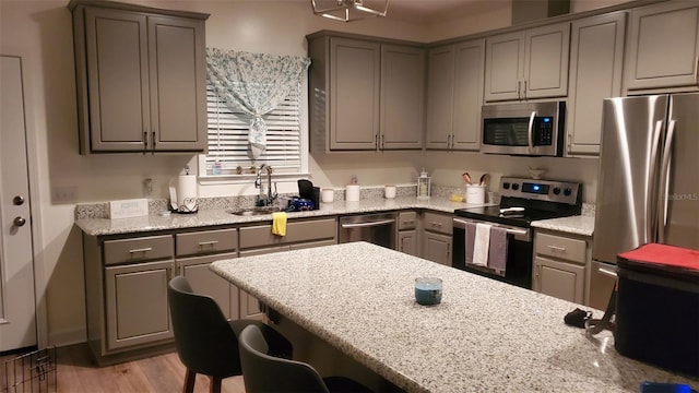 kitchen with appliances with stainless steel finishes, light wood-type flooring, light stone counters, a breakfast bar, and sink