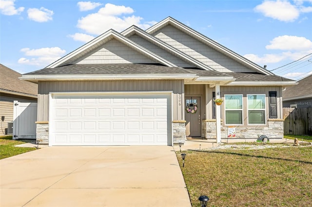 view of front of property featuring a garage, driveway, a shingled roof, stone siding, and a front lawn