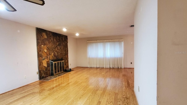 unfurnished living room with ceiling fan, light hardwood / wood-style floors, and a stone fireplace