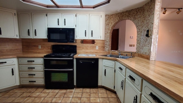 kitchen with white cabinets, sink, light tile patterned flooring, and black appliances