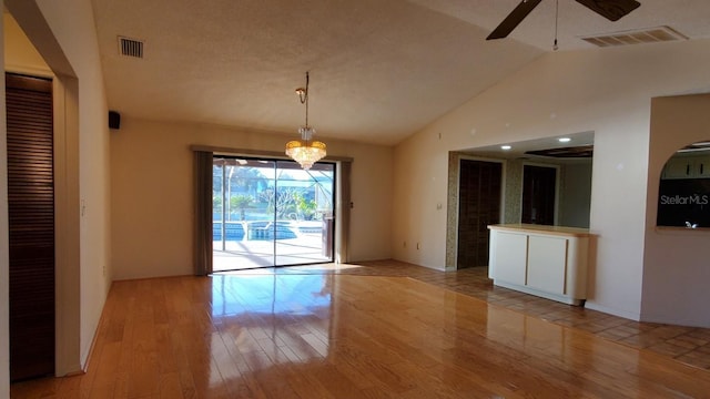 unfurnished dining area with a textured ceiling, ceiling fan with notable chandelier, lofted ceiling, and light wood-type flooring