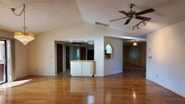 empty room with a textured ceiling, ceiling fan with notable chandelier, light hardwood / wood-style floors, and lofted ceiling