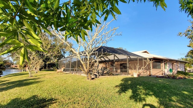 back of property with glass enclosure, a water view, and a yard