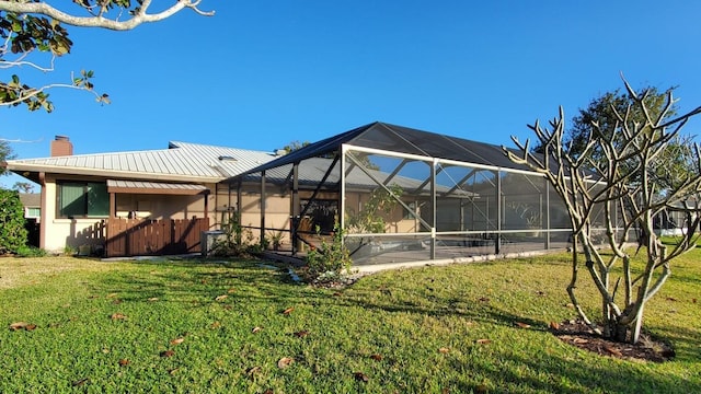 rear view of property featuring a lawn and glass enclosure