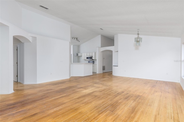 unfurnished living room with vaulted ceiling, a textured ceiling, a notable chandelier, and light wood-type flooring