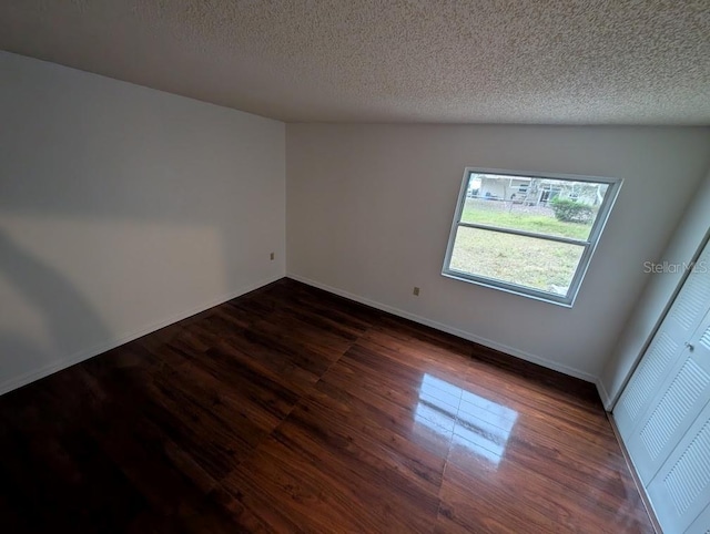 empty room with a textured ceiling, lofted ceiling, and dark hardwood / wood-style floors