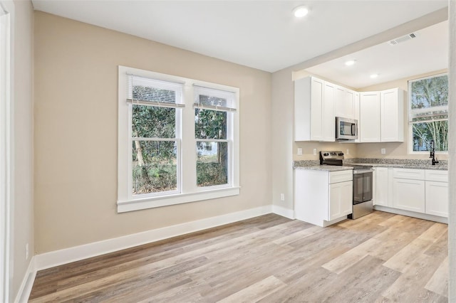 kitchen featuring white cabinets, stainless steel appliances, light hardwood / wood-style flooring, and light stone countertops