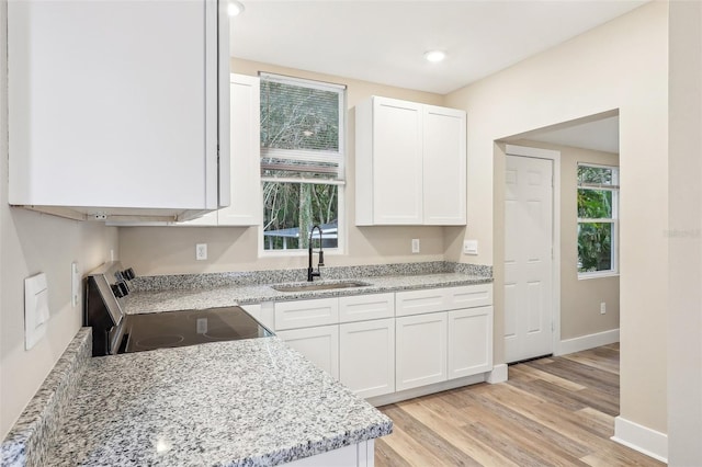 kitchen featuring a wealth of natural light, white cabinetry, sink, stainless steel stove, and light wood-type flooring