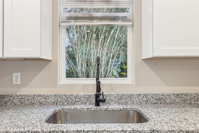 interior details with white cabinetry, light stone countertops, and sink