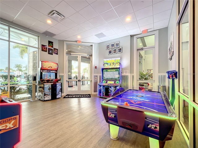 rec room with a paneled ceiling, a wealth of natural light, french doors, and wood-type flooring