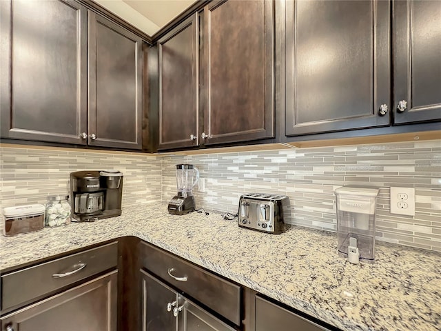 kitchen featuring dark brown cabinets, light stone counters, and backsplash