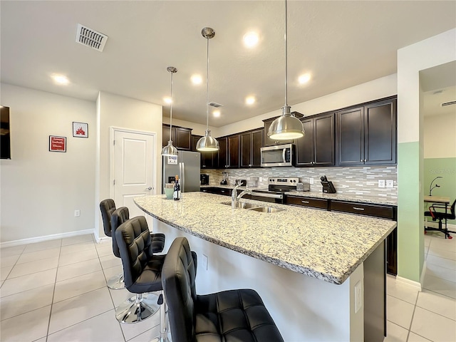 kitchen with appliances with stainless steel finishes, a center island with sink, light tile patterned floors, and pendant lighting