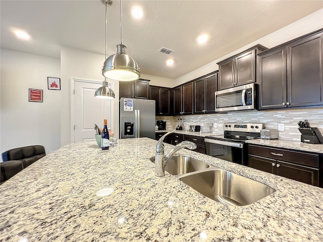 kitchen with light stone countertops, dark brown cabinetry, stainless steel appliances, sink, and hanging light fixtures