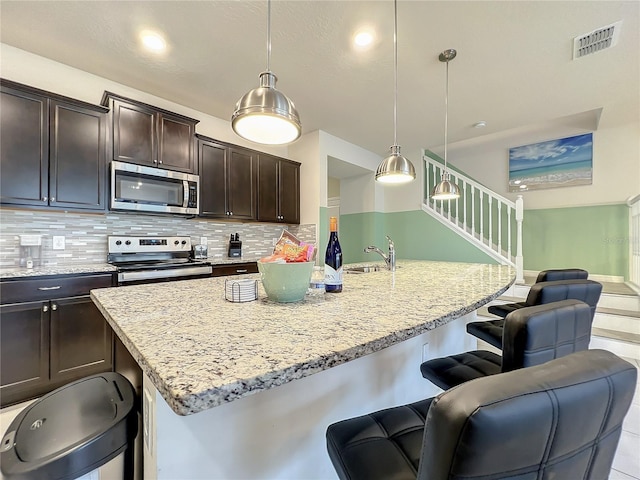 kitchen with hanging light fixtures, stainless steel appliances, and a center island with sink