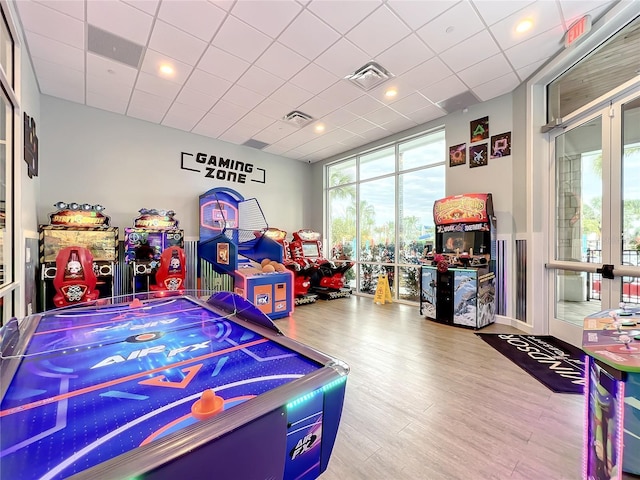 rec room featuring a wall of windows, hardwood / wood-style flooring, and a drop ceiling