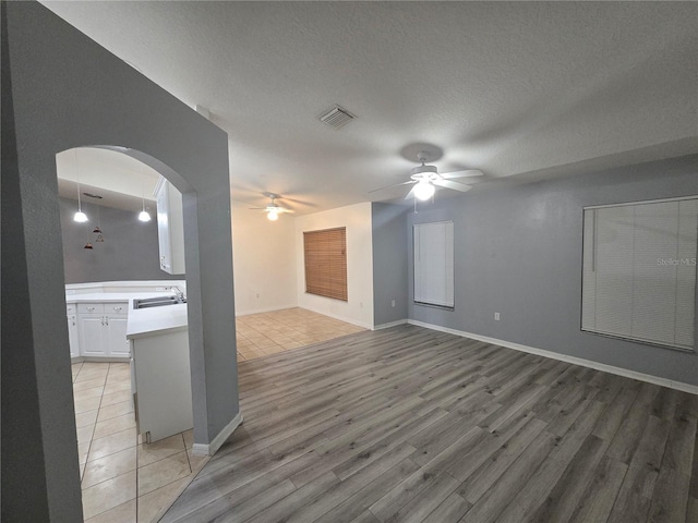 empty room with sink, a textured ceiling, ceiling fan, and light hardwood / wood-style floors