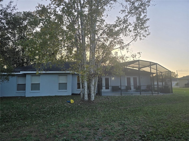 back house at dusk with a lawn, a lanai, and a patio