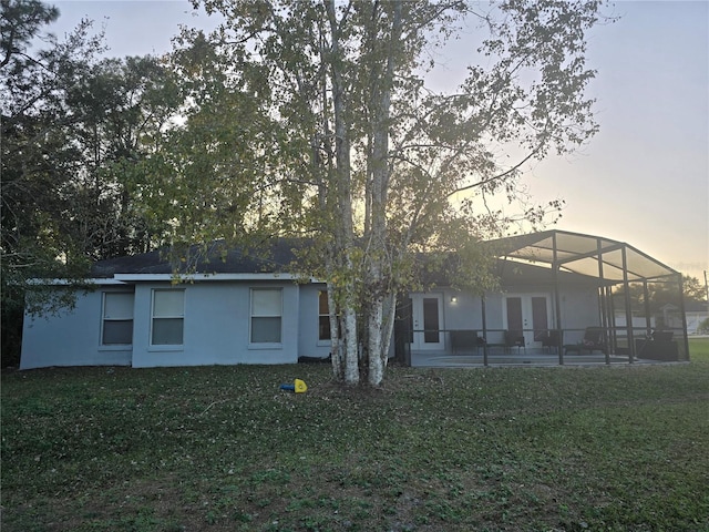 back house at dusk with a patio, glass enclosure, and a yard