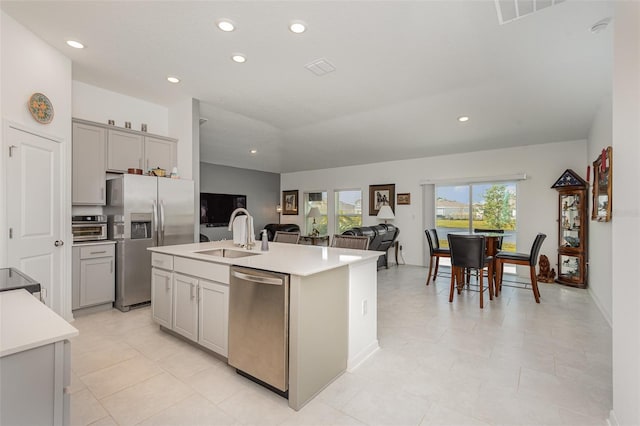 kitchen featuring a kitchen island with sink, sink, gray cabinets, light tile patterned floors, and appliances with stainless steel finishes