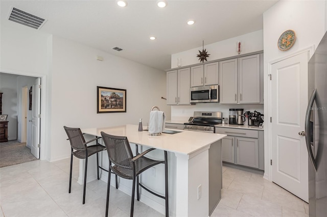 kitchen with gray cabinetry, a breakfast bar, a kitchen island with sink, and appliances with stainless steel finishes