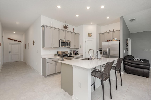 kitchen with sink, stainless steel appliances, a breakfast bar area, gray cabinets, and a kitchen island with sink