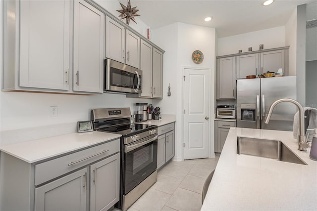 kitchen featuring gray cabinets, sink, light tile patterned floors, and appliances with stainless steel finishes