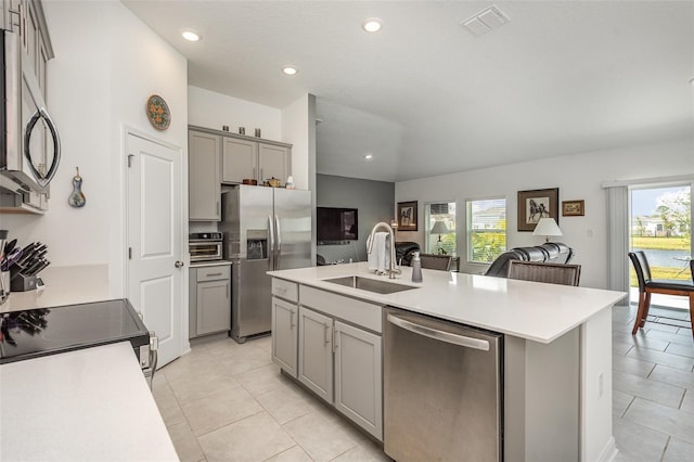 kitchen with a kitchen island with sink, sink, gray cabinets, light tile patterned floors, and stainless steel appliances