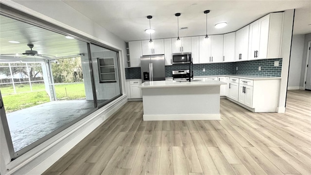 kitchen with a center island with sink, decorative light fixtures, white cabinets, and appliances with stainless steel finishes