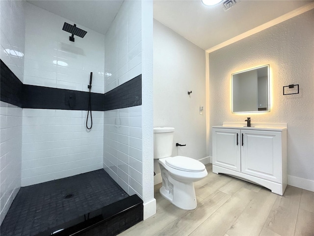 bathroom with hardwood / wood-style flooring, vanity, toilet, and tiled shower