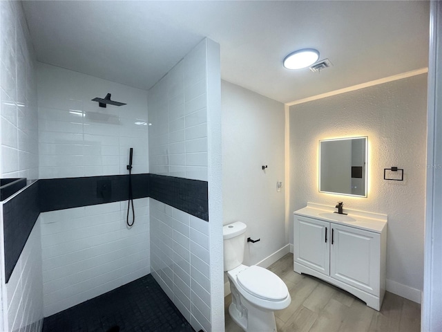 bathroom with vanity, tiled shower, hardwood / wood-style flooring, tile walls, and toilet