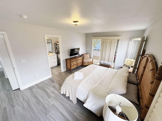 bedroom with ensuite bathroom, a textured ceiling, and light wood-type flooring