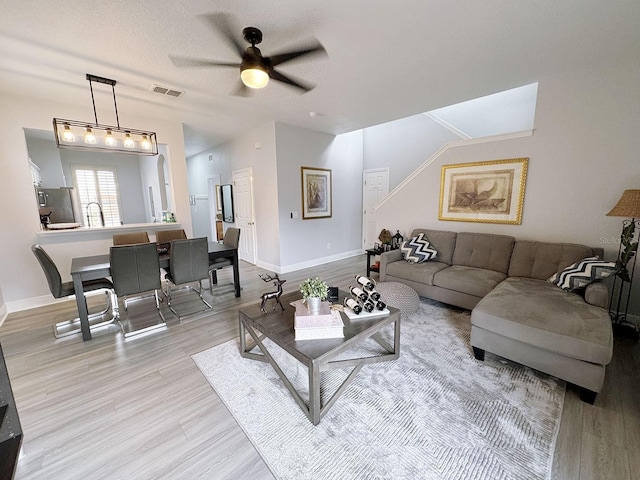 living room with ceiling fan, light hardwood / wood-style floors, and a textured ceiling