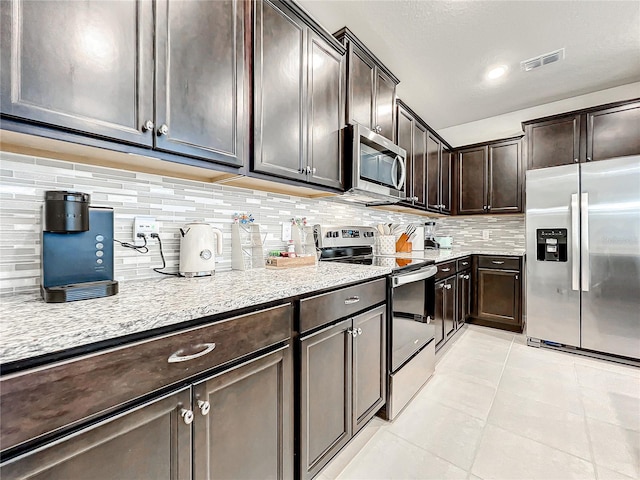 kitchen featuring light stone countertops, appliances with stainless steel finishes, backsplash, dark brown cabinets, and light tile patterned floors