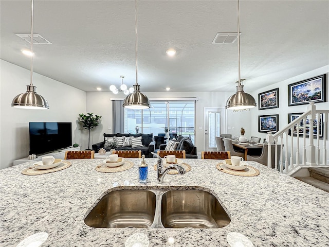 kitchen with a textured ceiling, decorative light fixtures, light stone counters, and sink