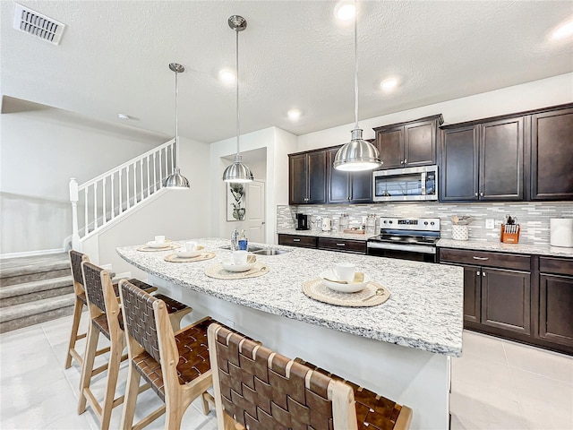 kitchen featuring sink, stainless steel appliances, pendant lighting, a textured ceiling, and a kitchen island with sink