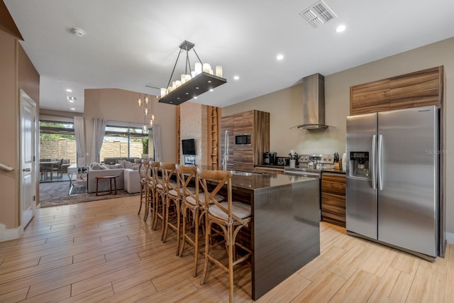 kitchen featuring a kitchen breakfast bar, wall chimney exhaust hood, stainless steel appliances, a kitchen island, and hanging light fixtures